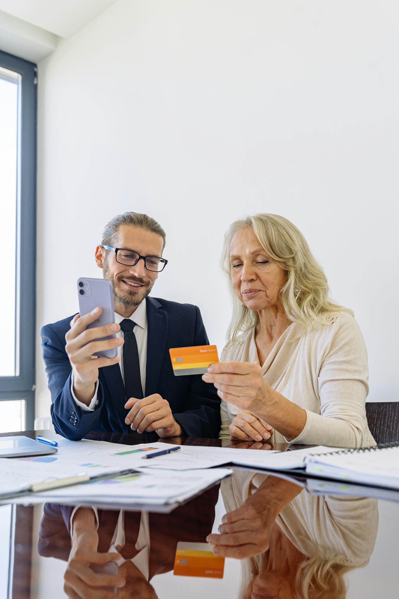 Senior woman and businessman discussing finance using smartphone and credit card in office.